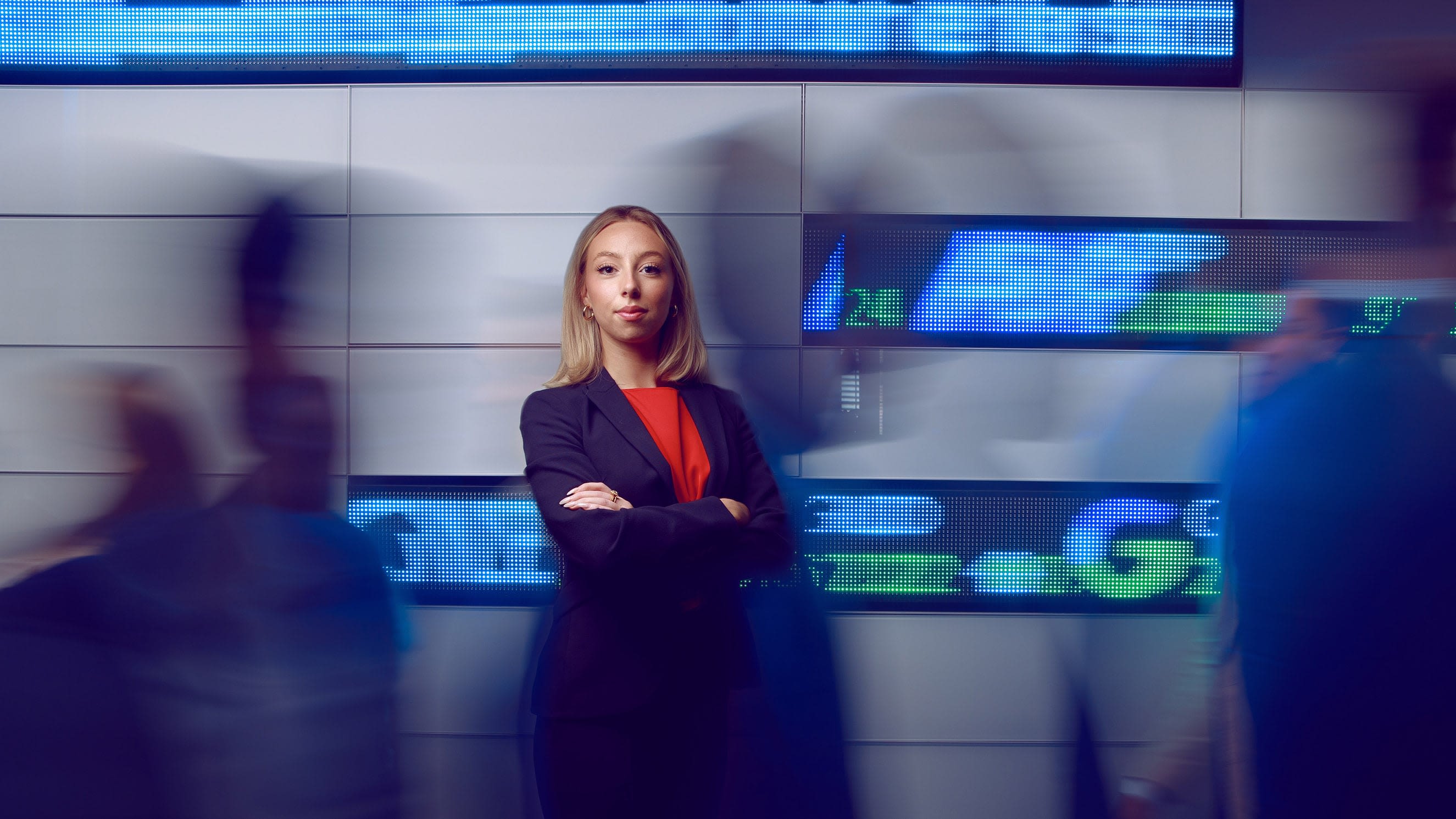 Ellery Hill stands in front of a digital stock ticker board.