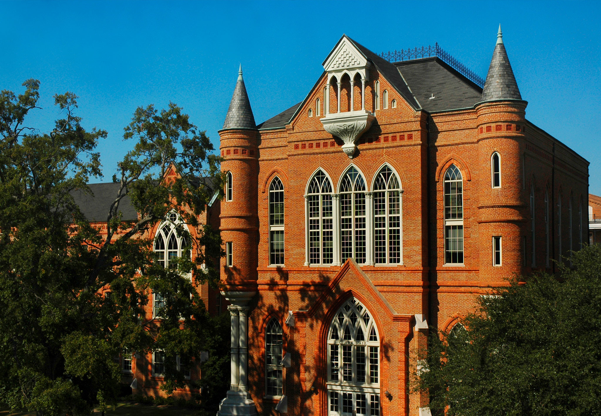 Clark Hall's red brick Gothic Revival facade, with pointed arch windows, conical turrets and a white balcony, framed by oak branches