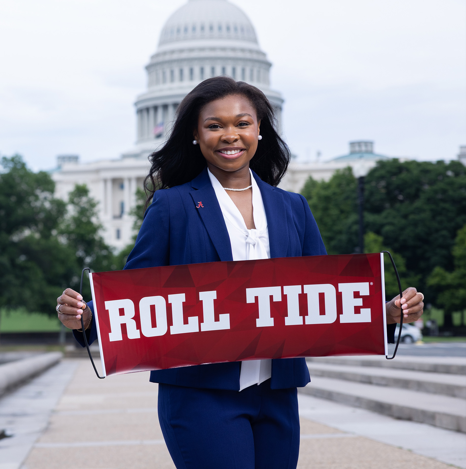 A student in a navy suit holds a crimson "Roll Tide" banner in front of the U.S. Capitol dome
