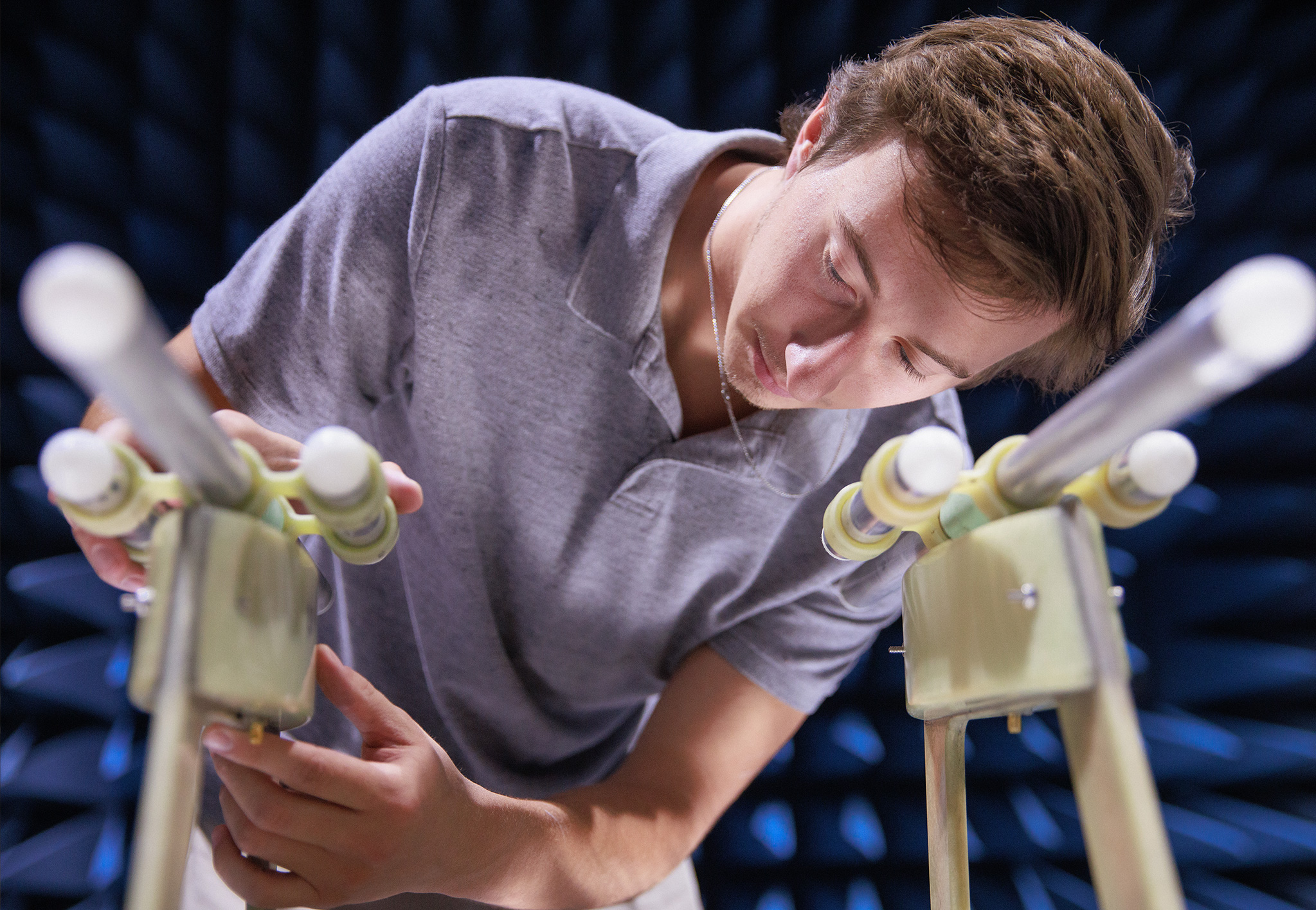 A student adjusts a pair of antenna assemblies inside an anechoic chamber lined with blue foam absorbers