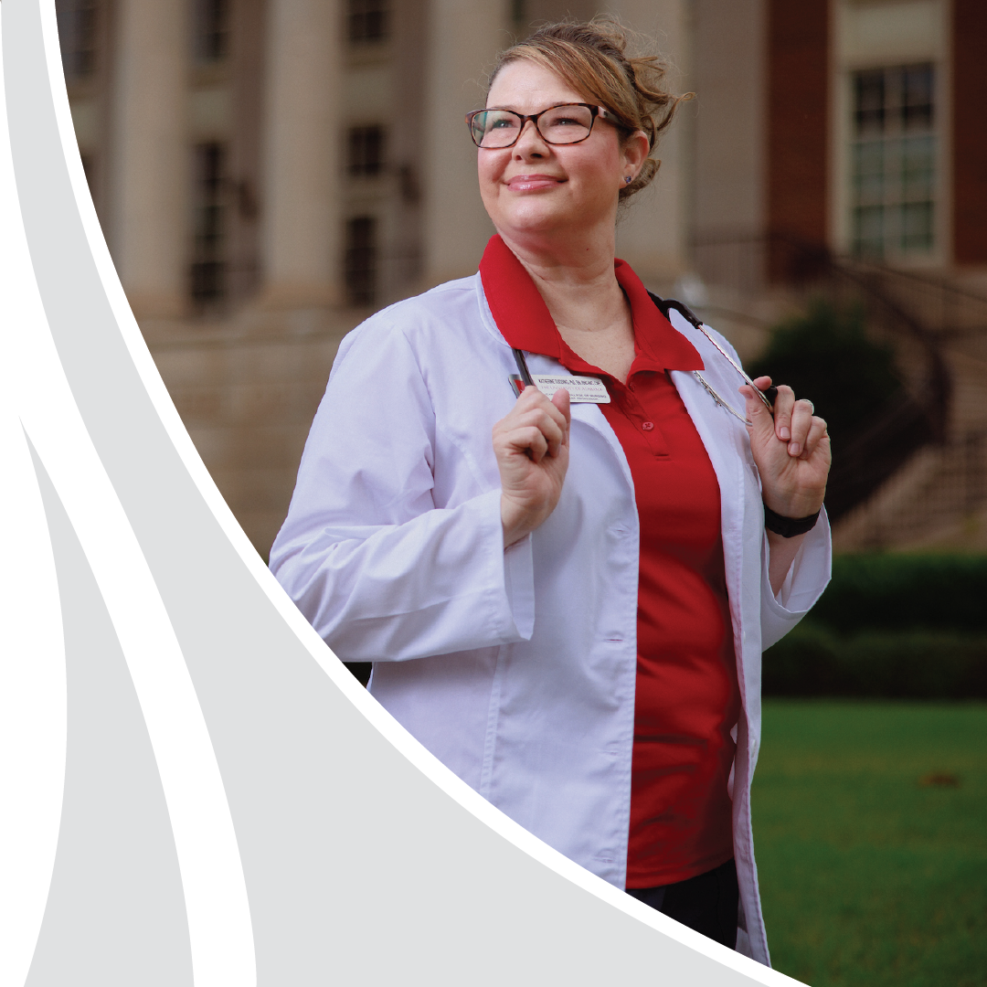 Dr. Dudding, a nursing faculty member in a white coat and crimson polo with a stethoscope, outside a columned campus building