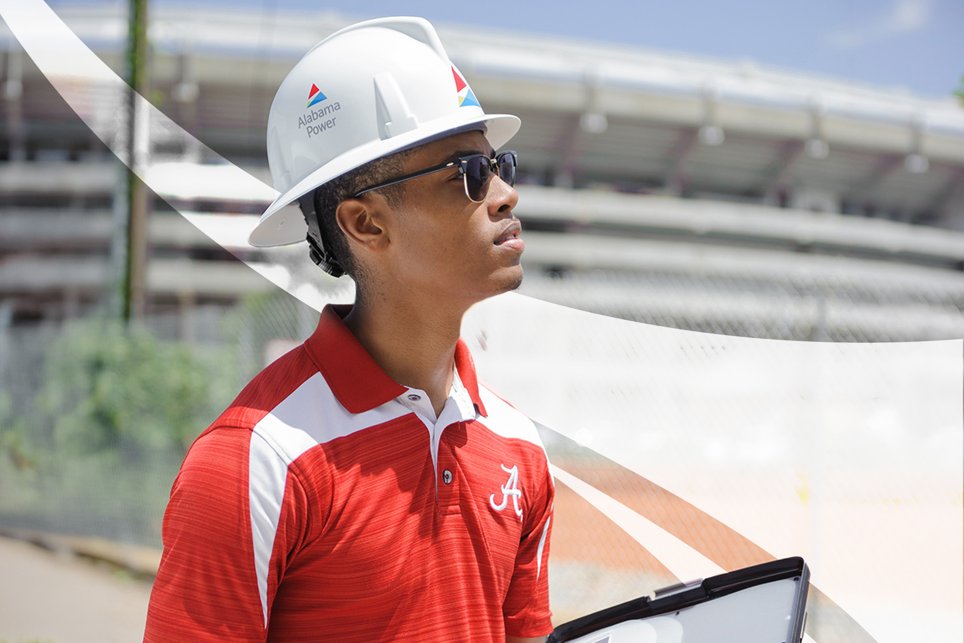 A student in an Alabama Power hard hat and crimson polo looks upward outside Bryant-Denny Stadium