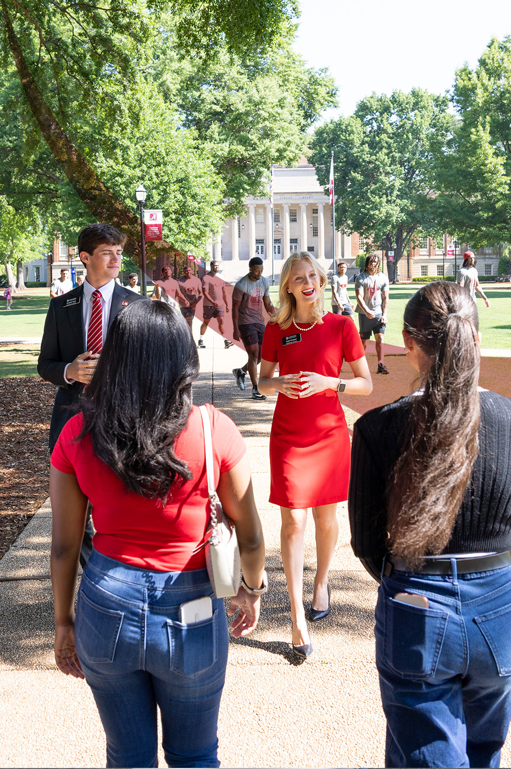 A tour guide in a red dress talks with prospective students on the Quad, Gorgas Library behind her