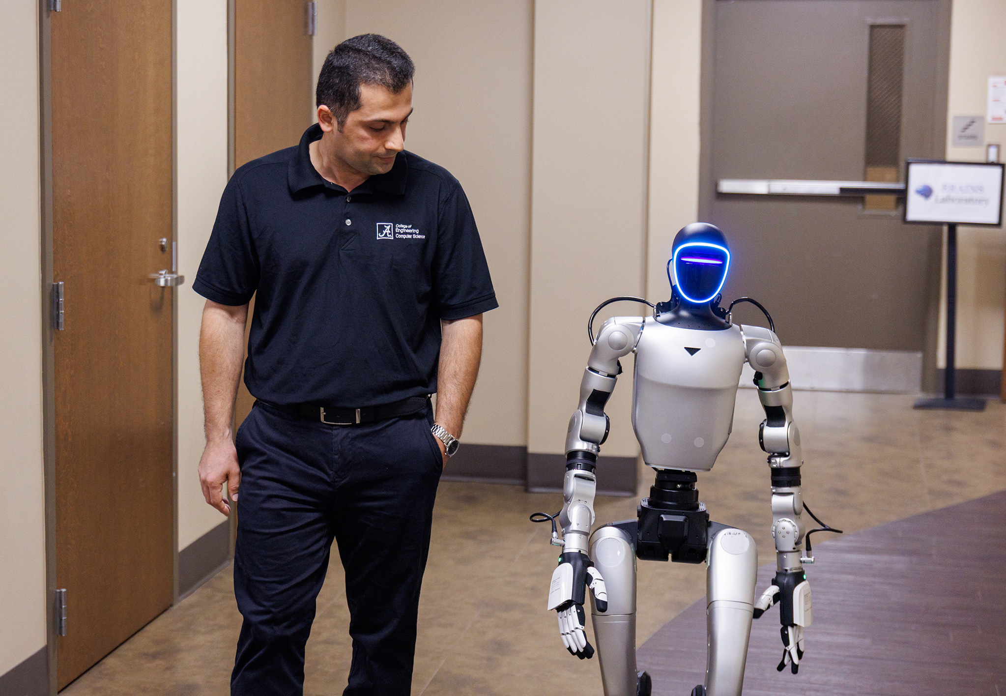 A College of Engineering faculty member walks alongside a humanoid robot down a building corridor