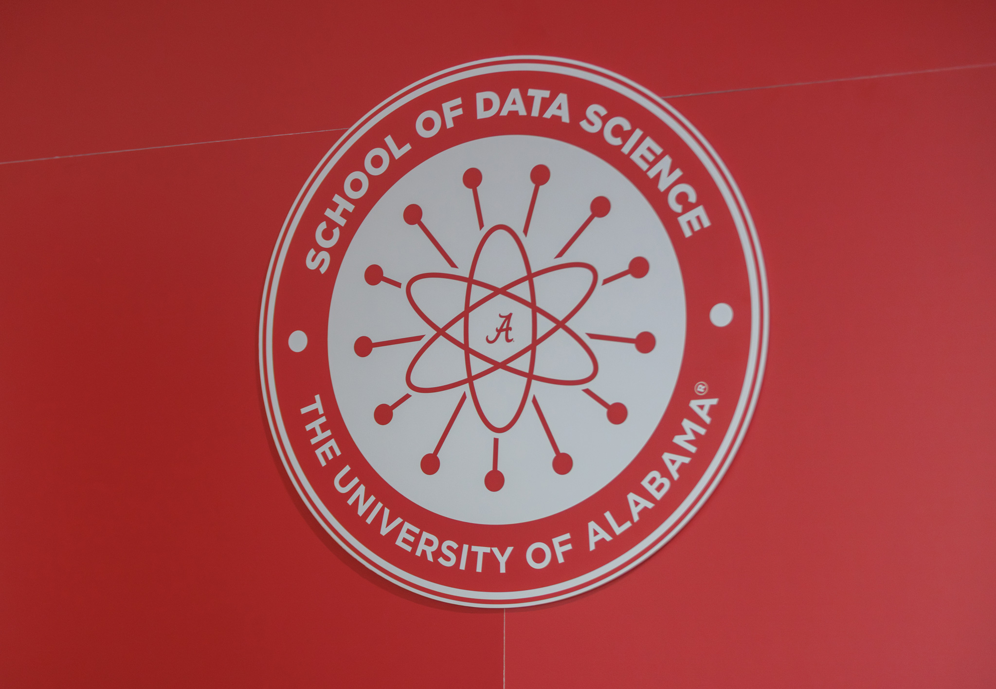 The School of Data Science seal — an atom encircling a script A — mounted on a crimson wall