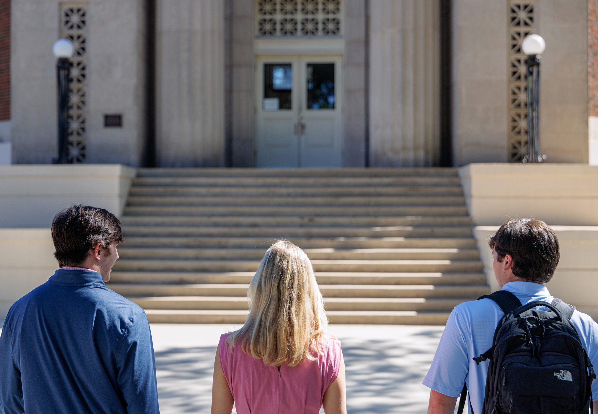 Three students seen from behind, facing the steps of a columned campus building